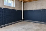 A basement wall drainage membrane and interior perimeter channel exposed before floor finishing