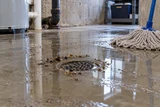 Standing clear water over a basement floor drain with a small debris line and wet mop nearby