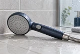 A handheld shower with a water-saving pause switch and a slim spray head resting on pale shower tiles, delicate water droplets