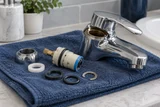Disassembled single-handle bathroom faucet cartridge and seals beside the chrome faucet body on a folded blue towel