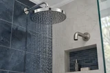 A polished chrome rainfall showerhead and brushed wall-mounted spout above a tiled shower niche