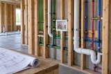 An unfinished house service wall with carefully routed supply and reuse pipework beside a rolled architectural plan