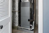 An unbranded residential air handler in a utility closet with insulated ductwork and condensate drain pipe