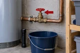 A clearly reachable household main shutoff wheel with a plain arrow-shaped marker, an emergency torch and bucket below