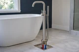 A new freestanding bathtub floor-mounted filler with its mounting base exposed and supply pipes rising through the floor