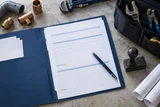 A permit document folder with blank forms, a pen and a municipal-style stamp beside an unbranded tool bag