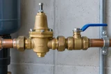 An installed brass pressure-reducing valve with adjustment screw and blue lever isolation valve on a horizontal water supply pipe