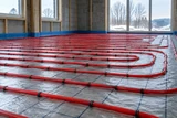 Red radiant floor heating tubing clipped in orderly loops across an unfinished floor before the concrete pour