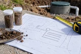 A septic site plan with simple illegible surveying marks beside soil samples and measuring tape outdoors