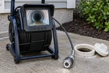 A sewer inspection camera reel with its small screen showing a pipe interior and camera head beside a cleanout