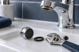 A loose faucet aerator beside a fresh washer and a small adjustable wrench on a bathroom sink ledge