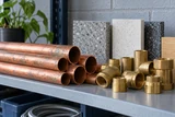 Recycled copper pipe lengths beside durable brass fittings and certified-style unmarked material samples on a workshop shelf