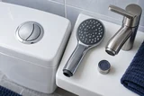 A modern dual-flush toilet button beside a flow-restricting showerhead and low-flow faucet insert on a white ceramic shelf